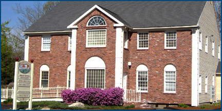 The image shows a two-story brick house with white trim, a front porch, and a red roof. There is a sign on the lawn that reads  THE HILL HOSPITAL.