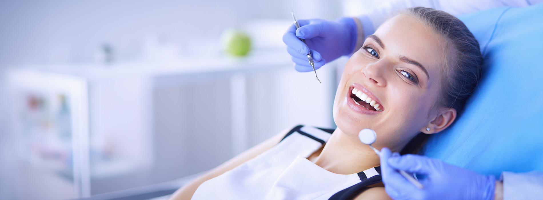 A woman receiving dental care, with a smile on her face and a dental hygienist in the background.