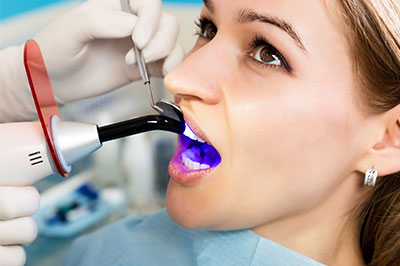 A woman in a dental chair receiving a teeth cleaning, with a dental hygienist using an electric toothbrush and spraying water into her mouth.