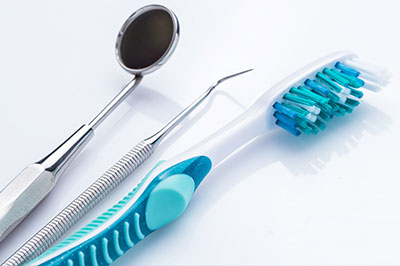 The image shows a collection of dental tools, including a toothbrush and dental instruments such as tweezers, on a white background.