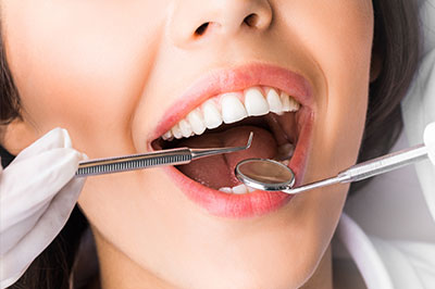 A smiling woman in a dental office, holding a toothbrush and showing her teeth while wearing a white coat.