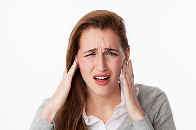 The image shows a woman with her hand on her head, possibly indicating pain or discomfort. She is wearing a light-colored top and has dark hair.