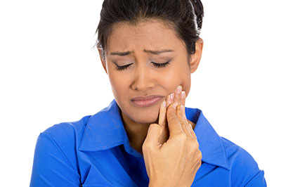 A woman in a blue shirt holding her face with one hand, displaying concern or discomfort.