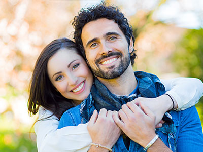 A man and woman embracing, smiling, and posing for a photo outdoors.