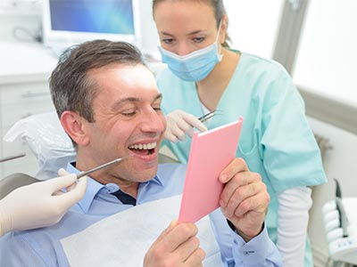 The image shows a person holding an open pink card in front of their face, surrounded by dental professionals who are smiling and appear to be engaged in a positive interaction.