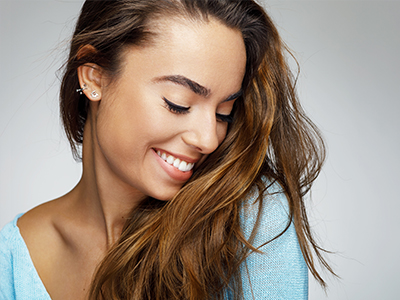 A smiling woman with long hair, wearing a blue top, posing against a white background.