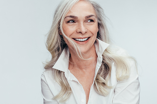 The image shows a woman with short hair, wearing a white shirt, smiling and looking directly at the camera.