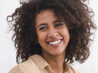 A smiling woman with curly hair, wearing a light-colored shirt, against a plain background.